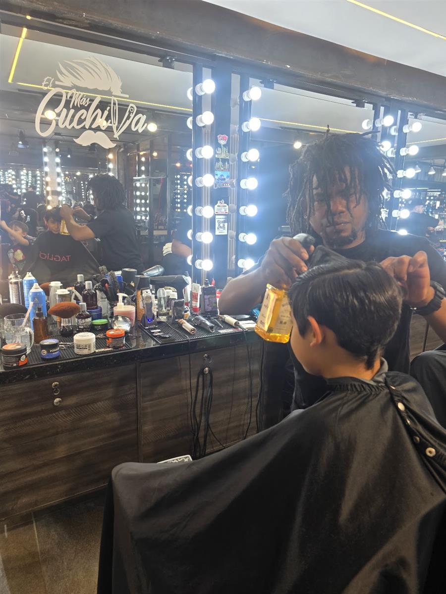 Barbero de TAGLIO cortando el cabello de un niño frente a espejo con bombillos