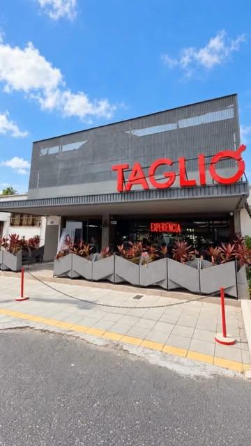Fachada de TAGLIO con su letrero rojo bajo el cielo azul