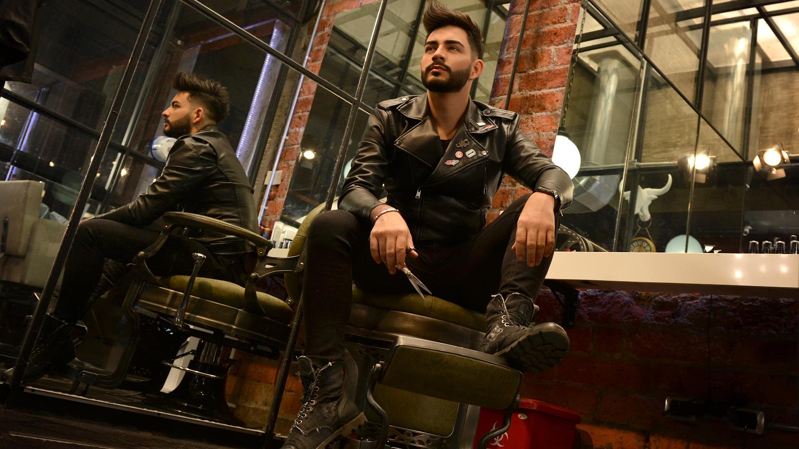 Interior de TAGLIO: hombre con chaqueta de cuero sentado en silla de barbero junto a la vitrina