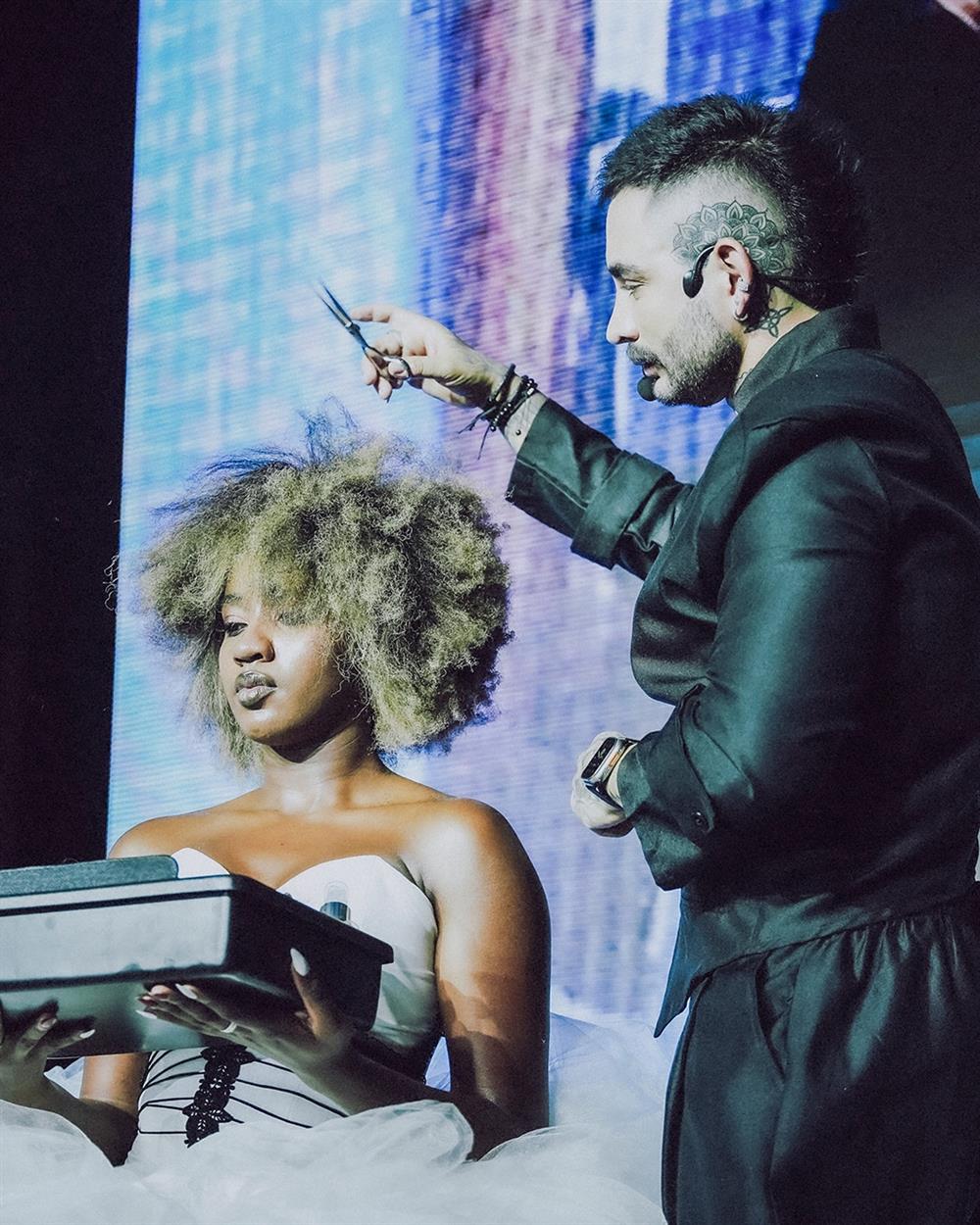 Estilista esculpiendo un afro rubio a una modelo en escena